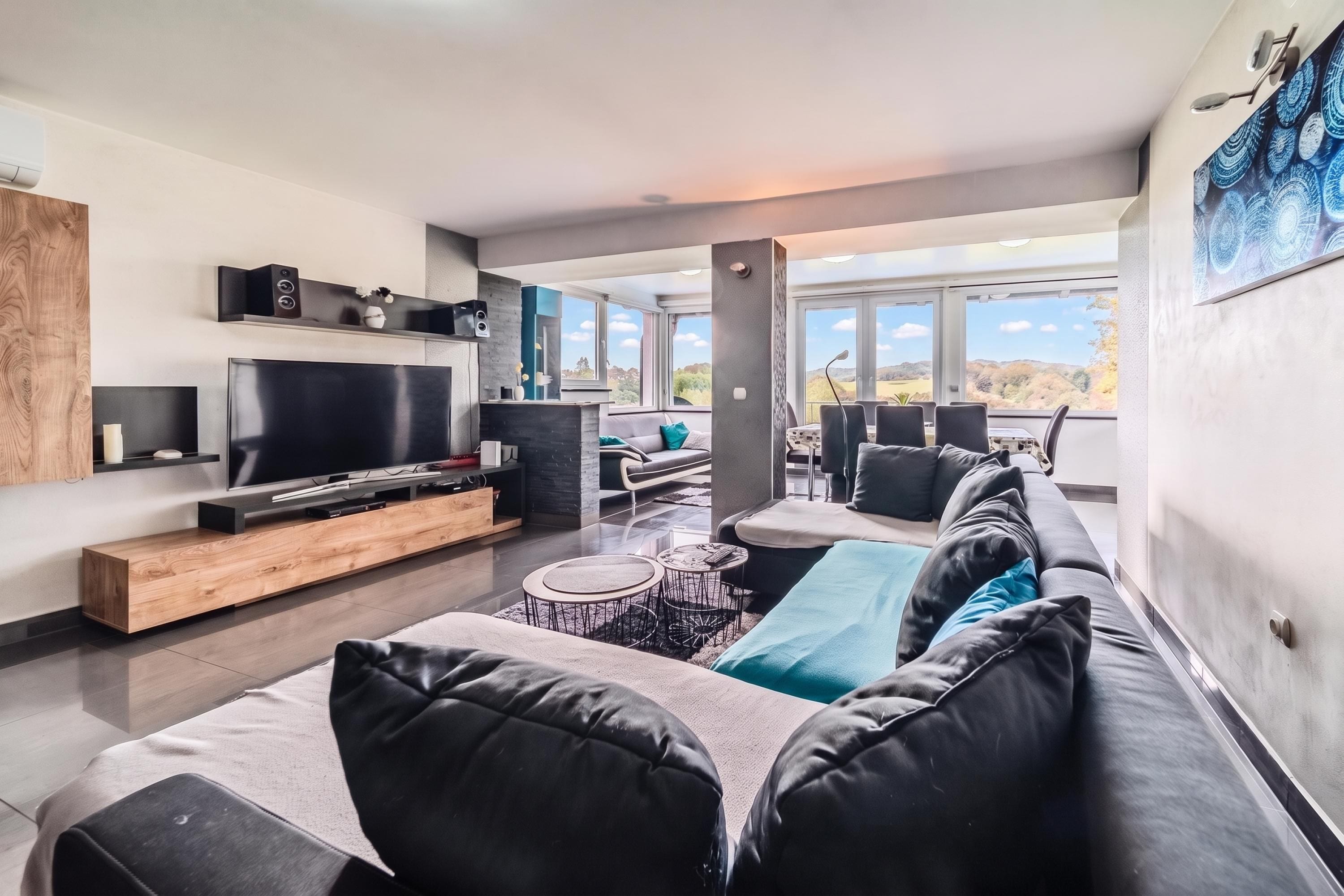 A modern living room with a flat-screen TV, a sofa, a coffee table, and a dining area with chairs.