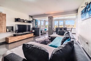 A modern living room with a flat-screen TV, a sofa, a coffee table, and a dining area with chairs. - Riverside House With Pool and Hot Tub (Karlovac)