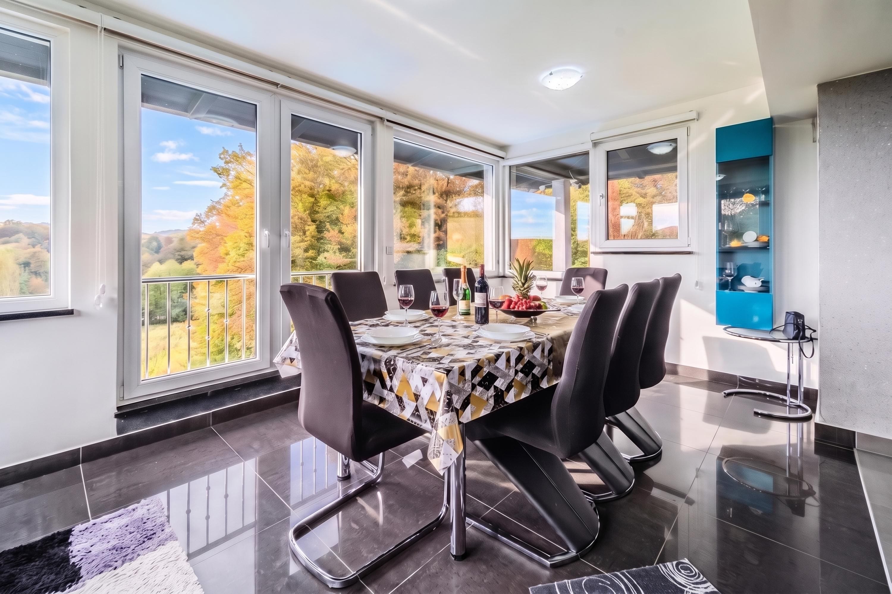 Un comedor con una mesa dispuesta para seis personas, ventanas amplias y vistas del follaje otoñal.