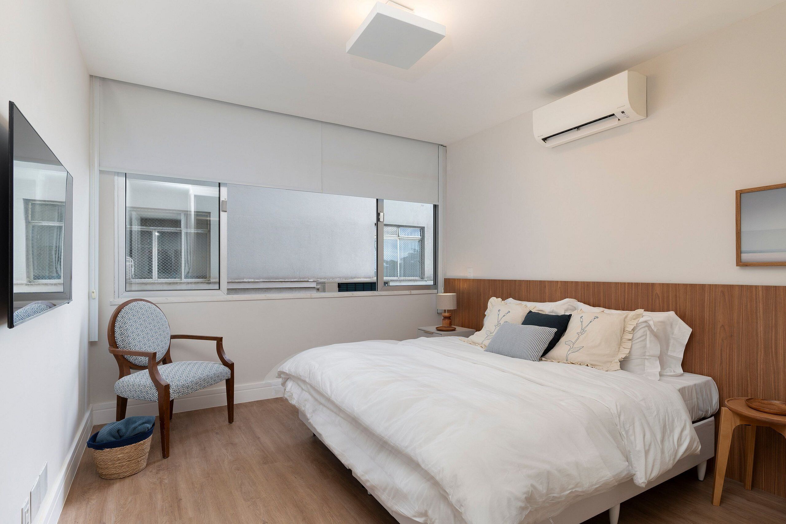 Une chambre à coucher avec un grand lit, une chaise en bois, une petite table et une fenêtre avec des stores.