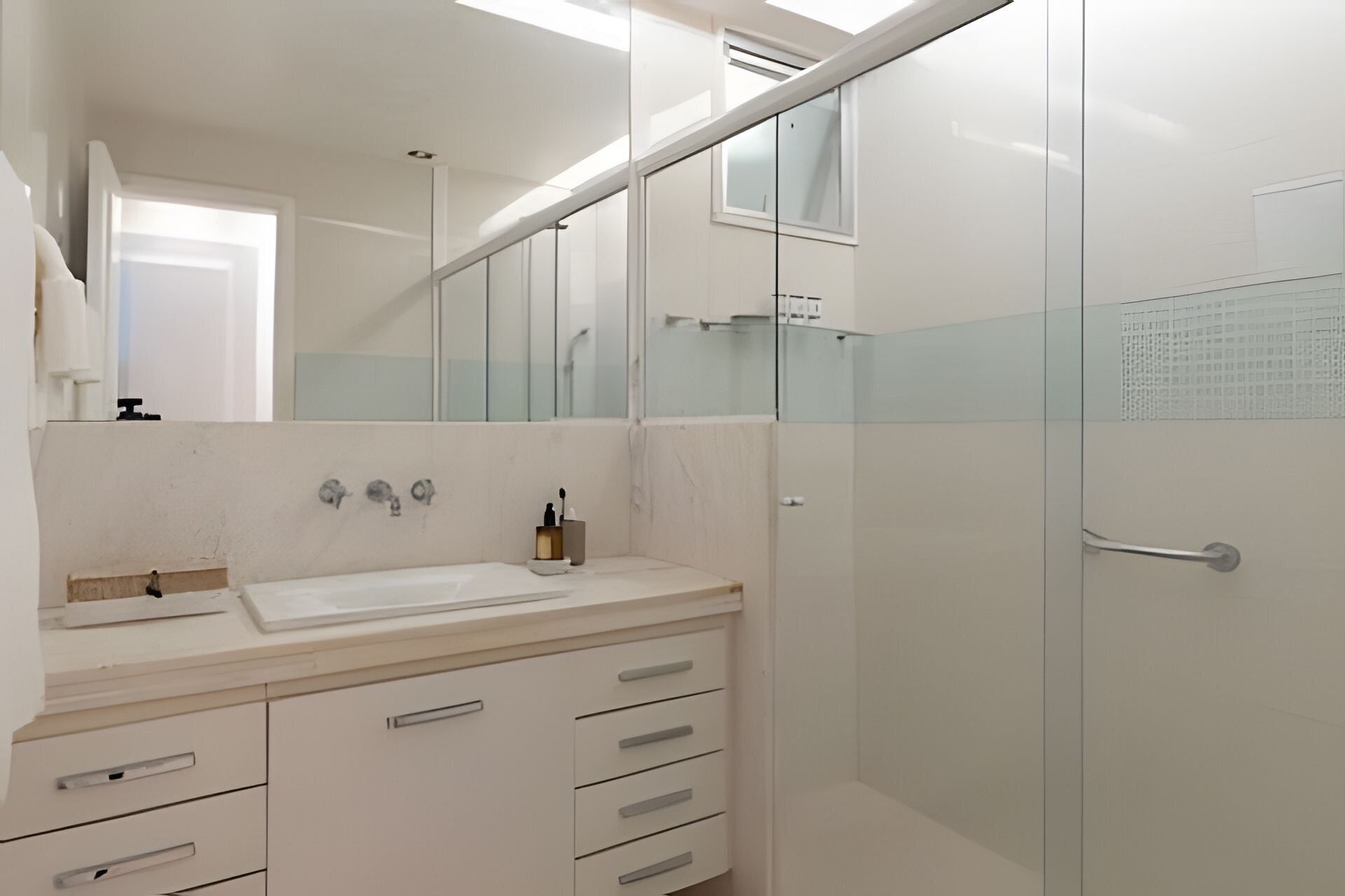Une salle de bain moderne avec un lavabo blanc, un miroir et une douche en verre.