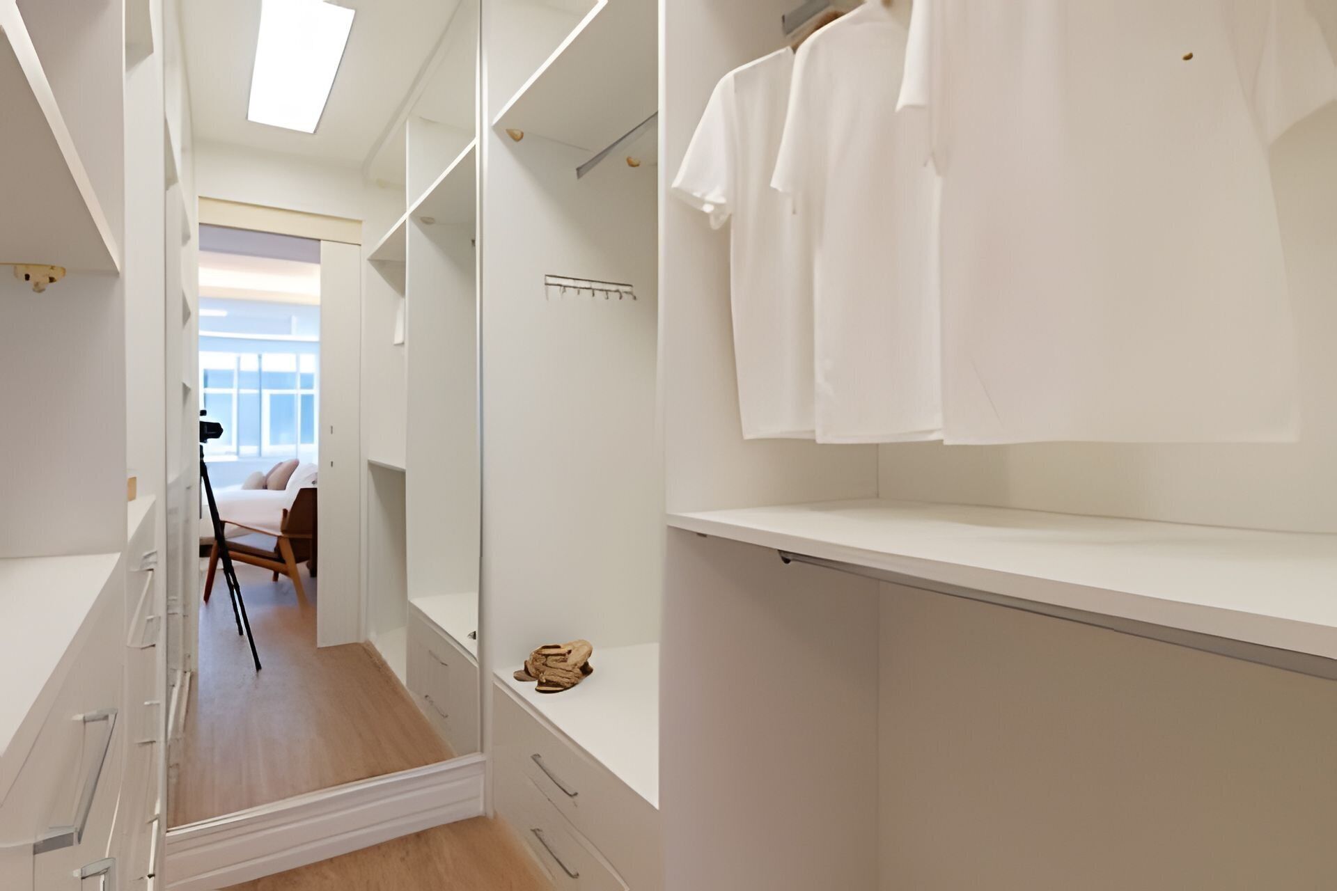 Ein begehbarer Kleiderschrank mit offenen Regalen, einem Spiegel und einem Stuhl im Hintergrund.