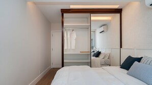 Ein modernes Hotelzimmer mit einem großen Bett, einem begehbaren Kleiderschrank und einem Spiegel über dem Bett.