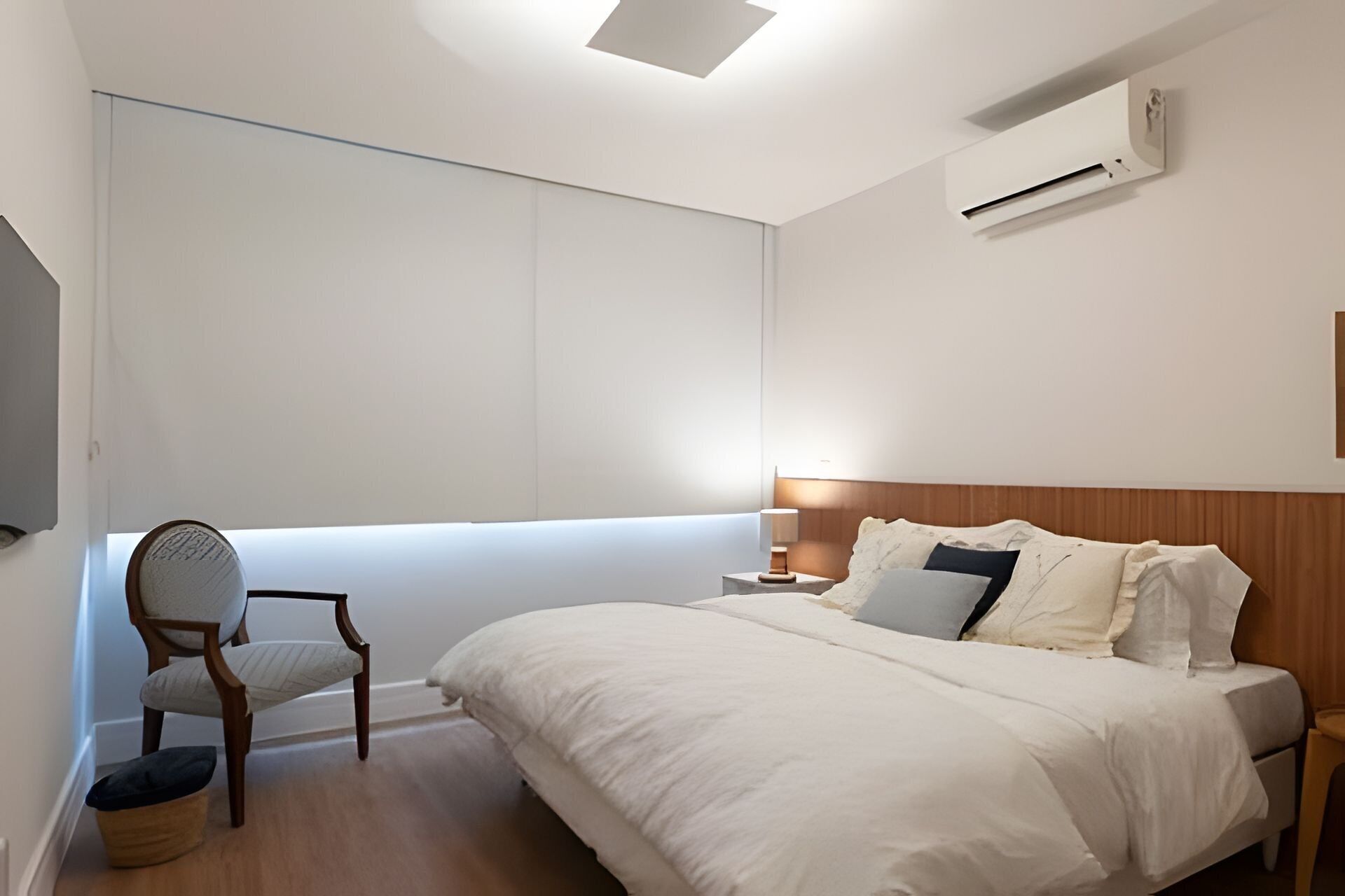 Een moderne hotelkamer met een groot bed, een stoel, een nachtkastje met een lamp en een airconditioner aan de muur.