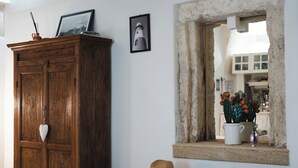 Une armoire en bois, un tableau encadré, une fenêtre donnant sur un paysage et un chapeau posé sur une table.