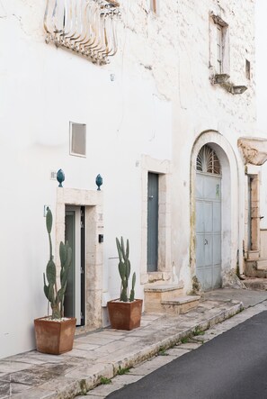 A narrow street with a white building featuring a door, a window, and a small balcony. There are two potted cacti in front of the building. - La casa di Laura, accogliente dimora nell'affascinante Ostuni, la "Città Bianca" (Ostuni)