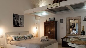 Une chambre avec un lit, une armoire en bois, une table en verre avec un verre à vin, et une pancarte « Bienvenue » au-dessus du lit.