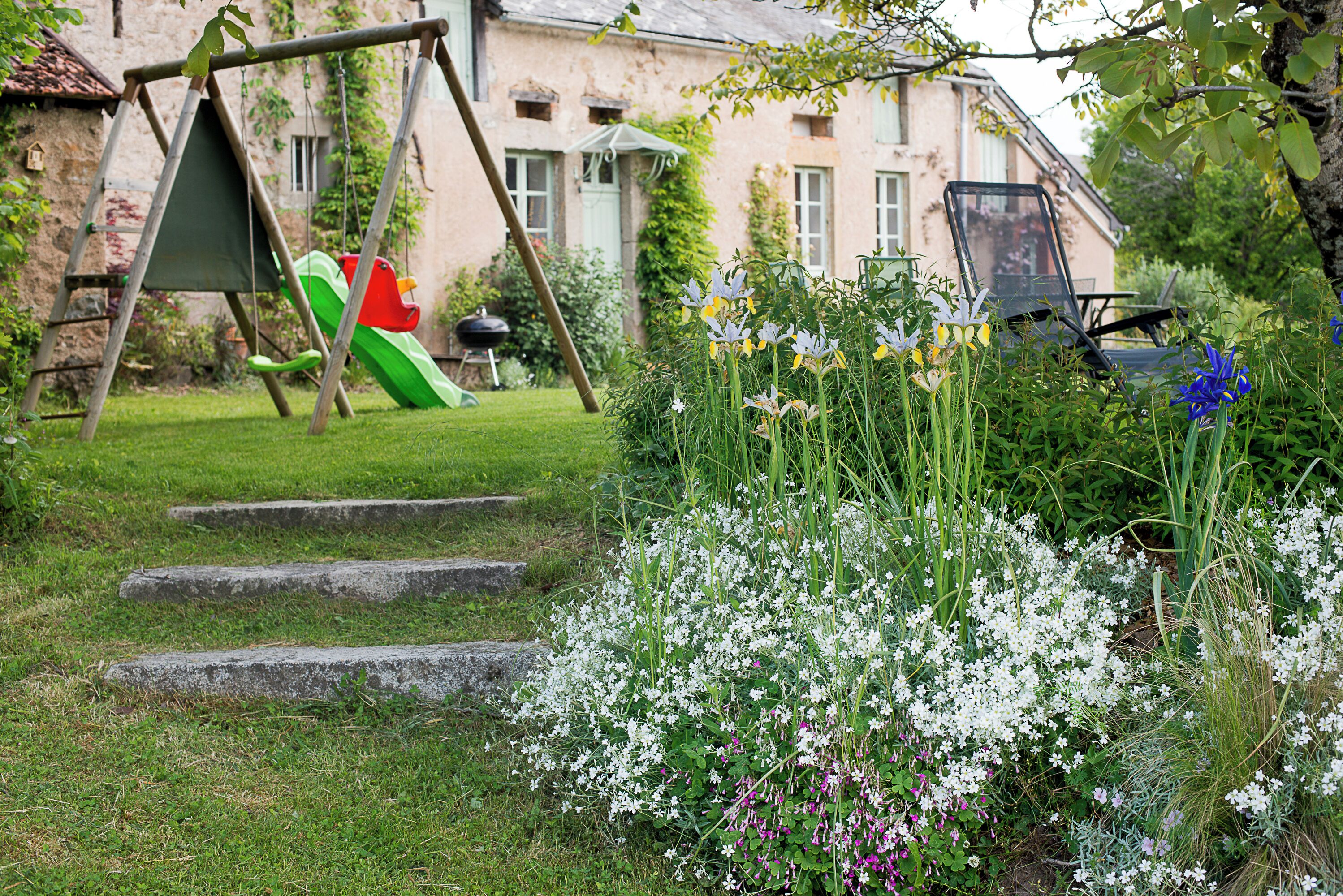 Un jardín con un columpio, un tobogán y diversas flores.