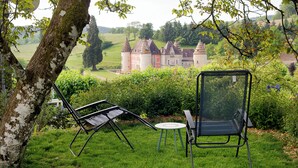 Ein Garten mit Schaukelstuhl und Tisch, umgeben von viel Grün und einem Blick auf eine Burg in der Ferne.
