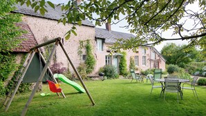 Ein Garten mit Schaukel, Esstisch und Stühlen sowie ein Haus mit Ziegelaußenwand.