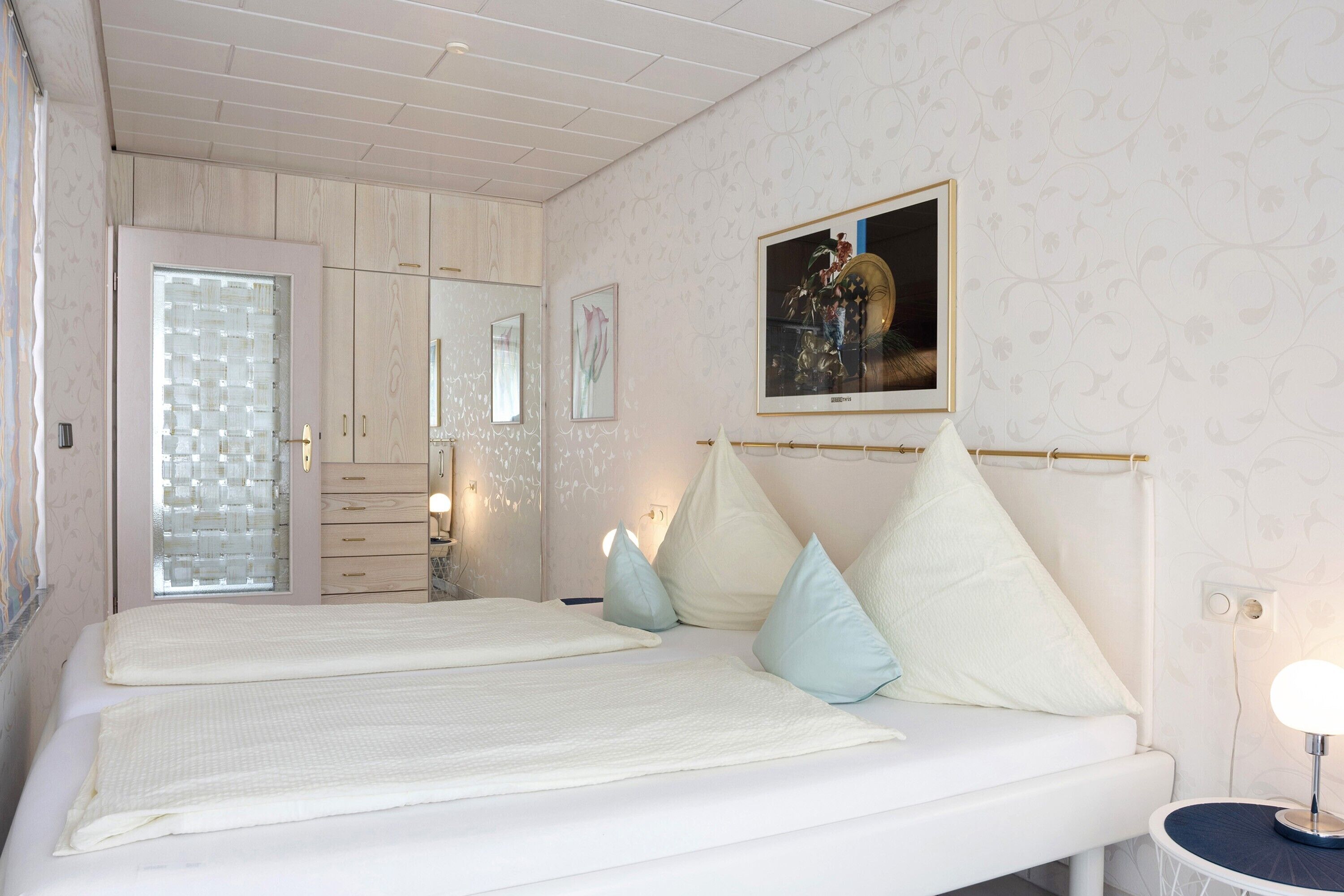 Ein Schlafzimmer mit einem großen Bett, einem Nachttisch mit Lampe, einem Kleiderschrank und einem Spiegel.