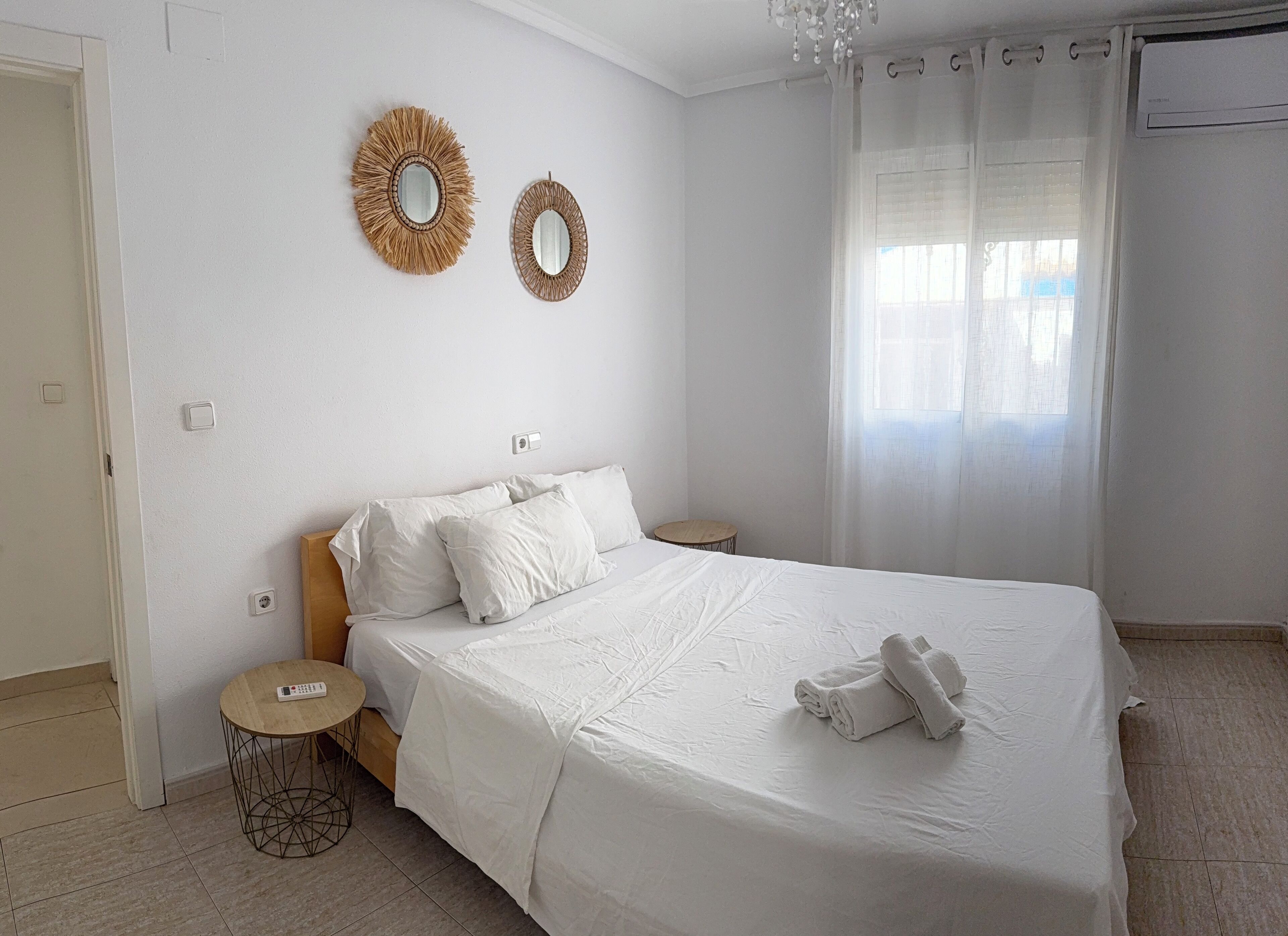 Un dormitorio con una cama grande, dos espejos en la pared, una mesita redonda y una ventana con cortinas.