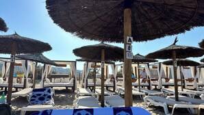 Una playa con filas de sillas de playa bajo sombrillas de paja, identificadas con letras y números.
