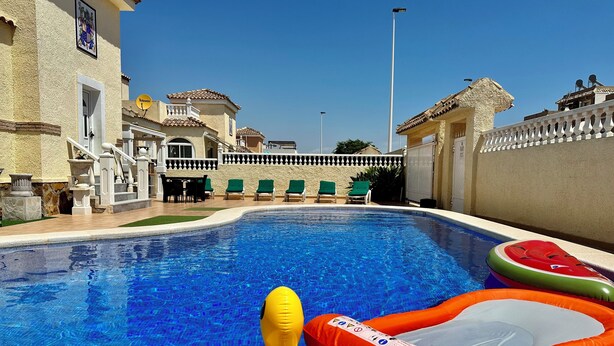 Una piscina con juguetes inflables, un porche cubierto y un edificio con balcón.