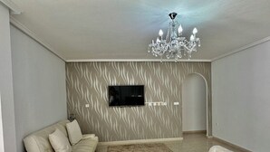 Una sala de estar moderna con un sofá seccional, un taburete tapizado, un televisor de pantalla plana montado en la pared y una araña.