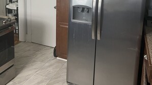 Ein Kühlschrank aus Edelstahl mit Wasserspender, Holzschränke und ein gefliester Boden in einer Küche.