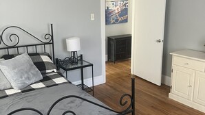 Ein Schlafzimmer mit Bett, Nachttisch, Lampe und einer Tür zu einem anderen Raum.