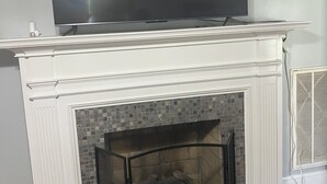Ein Kamin mit darüber montiertem Fernseher, einer gefliesten Umrandung und einer Glasschiebetür.