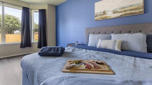 Ein Schlafzimmer mit einem Bett, einem Nachttisch, einem Gemälde und einem Frühstücksbrettchen auf dem Bett.