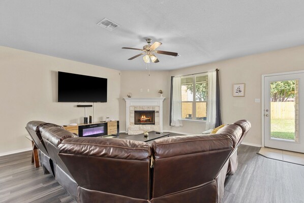 A living room with a fireplace, leather sofas, a flat-screen TV, and a ceiling fan.