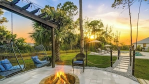 A patio area with a fire pit, hanging chairs, and a pool.