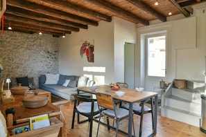 Un salon chaleureux avec un mur en pierre, un plafond en bois et une table à manger avec des chaises.