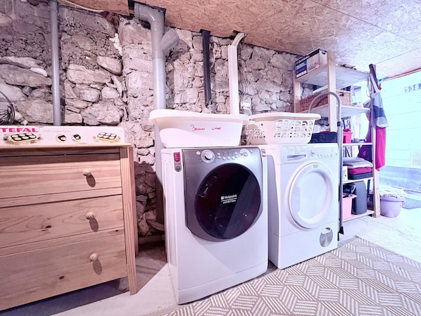 A laundry area with two washing machines, a wooden cabinet, and a stone wall.