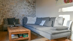 En stue med en stenvæg, en grå sofa, et træbord og en lille skildpaddefigur.