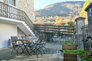 Un bâtiment en pierre doté d’un balcon, d’un espace extérieur aménagé pour s’asseoir et offrant une vue sur un paysage montagneux.