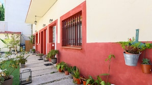 Un étroit sentier bordé de plantes en pot et un bâtiment aux murs rouges et blancs.