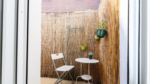Un petit espace extérieur aménagé avec une chaise et une table blanches, le tout entouré d’une clôture en bambou.
