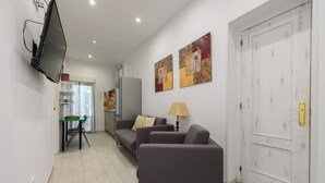 A modern living room with a sofa, a table, and a TV mounted on the wall. There are two paintings on the wall and a door with a handle. - M Sfu71 Acogedor Piso con Terraza y Espacios par (Madrid)