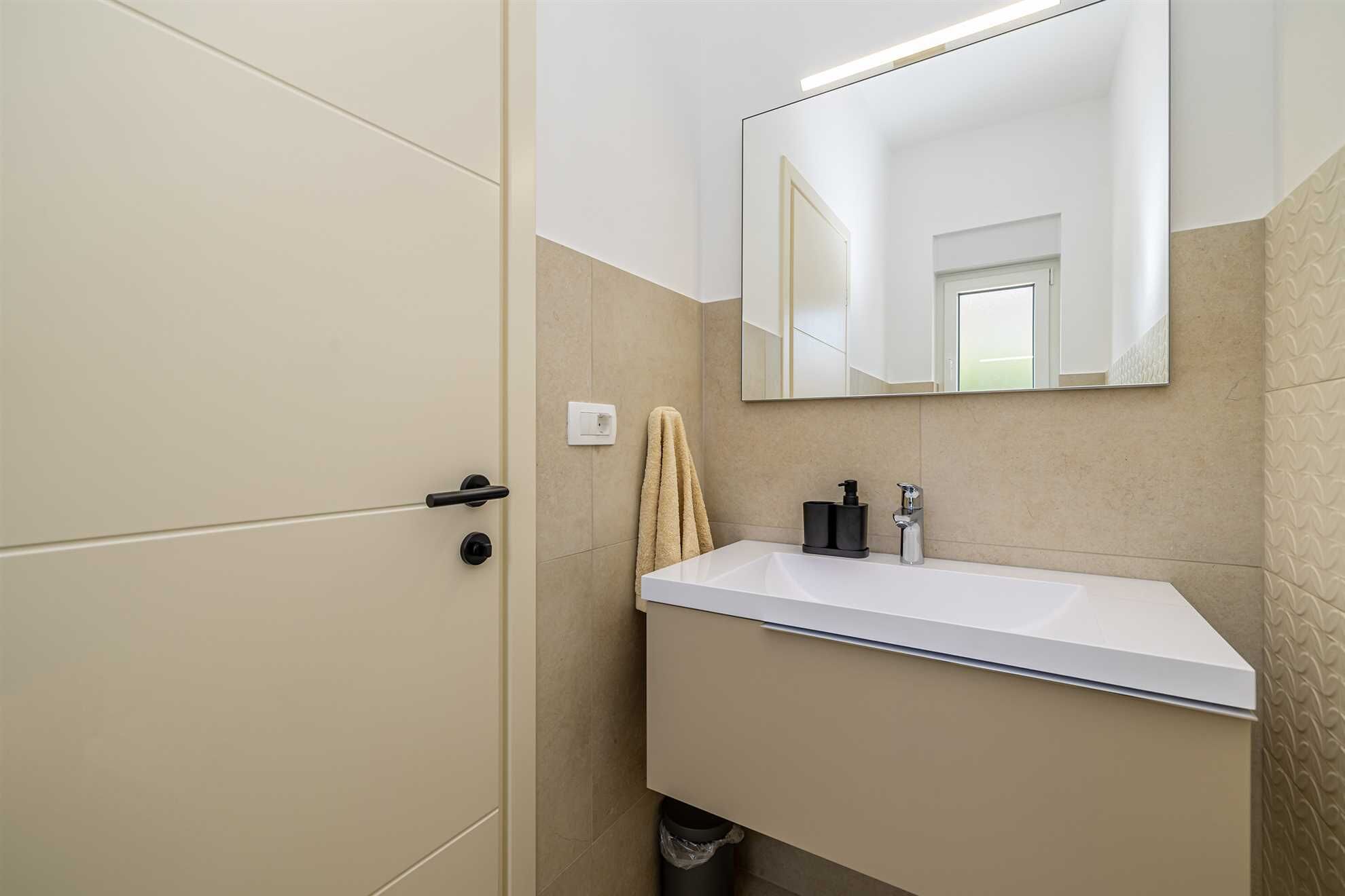 Un baño con un lavamanos blanco, un espejo y una toalla colgada en la pared.