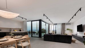 A modern living room with a large black sofa, a dining area with wooden chairs, and a kitchen with a bar.