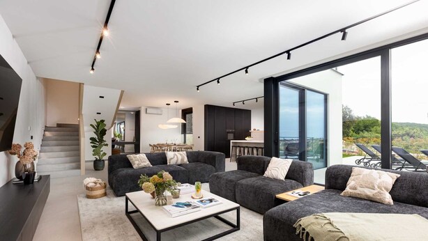 A modern living room with a sofa set, a coffee table, and a view of the kitchen and dining area.