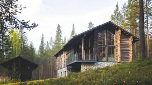 A log cabin with a balcony, surrounded by forest.