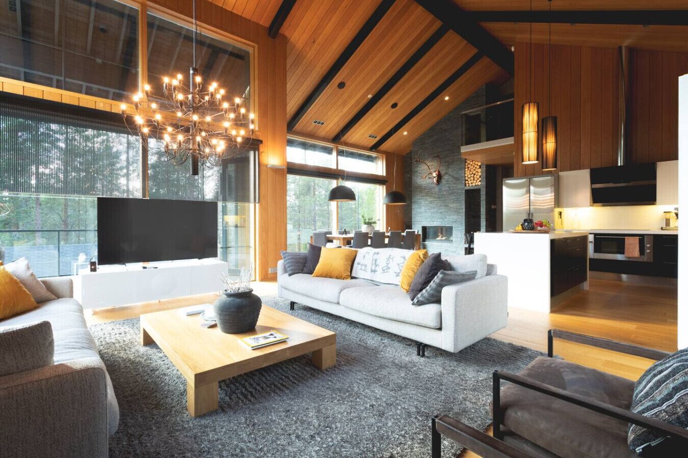Una sala de estar moderna con un sofá grande, una mesa de centro y un televisor. Se observa una zona de cocina con estufa y armarios.