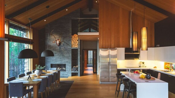 A modern kitchen with a large island, wooden beams, and a stone fireplace.