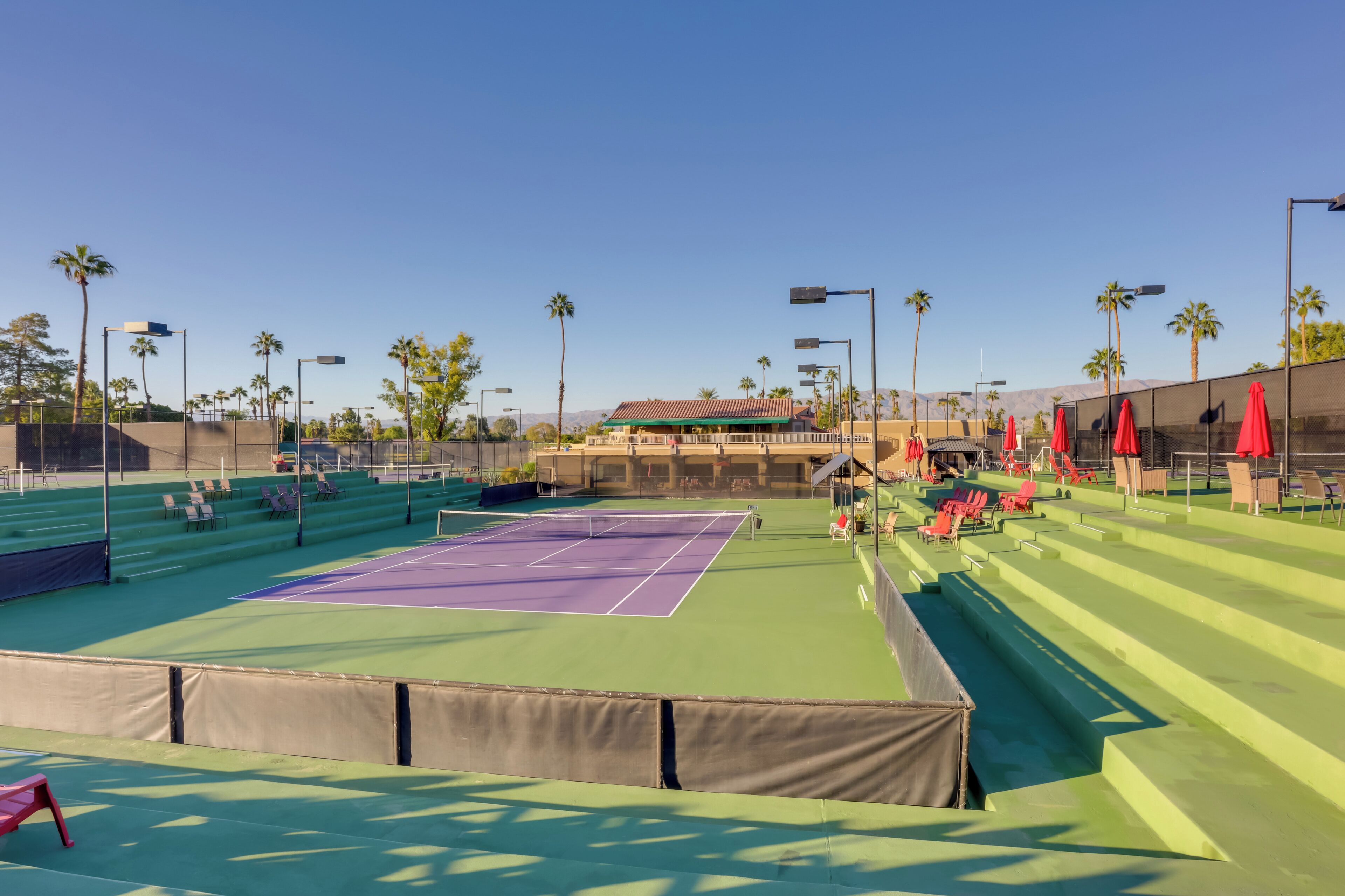 Un campo da tennis all'aperto con posti a sedere e palme.