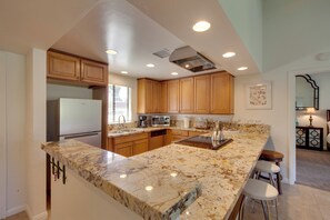 A modern kitchen with wooden cabinets, granite countertops, stainless steel appliances, and a bar area with stools.