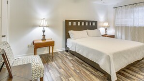 A neatly arranged bedroom with a bed, two bedside lamps, a wooden nightstand, a patterned chair, and a ceiling fan.