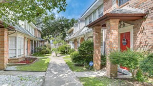 A residential street with brick houses, a clear sidewalk, and greenery.