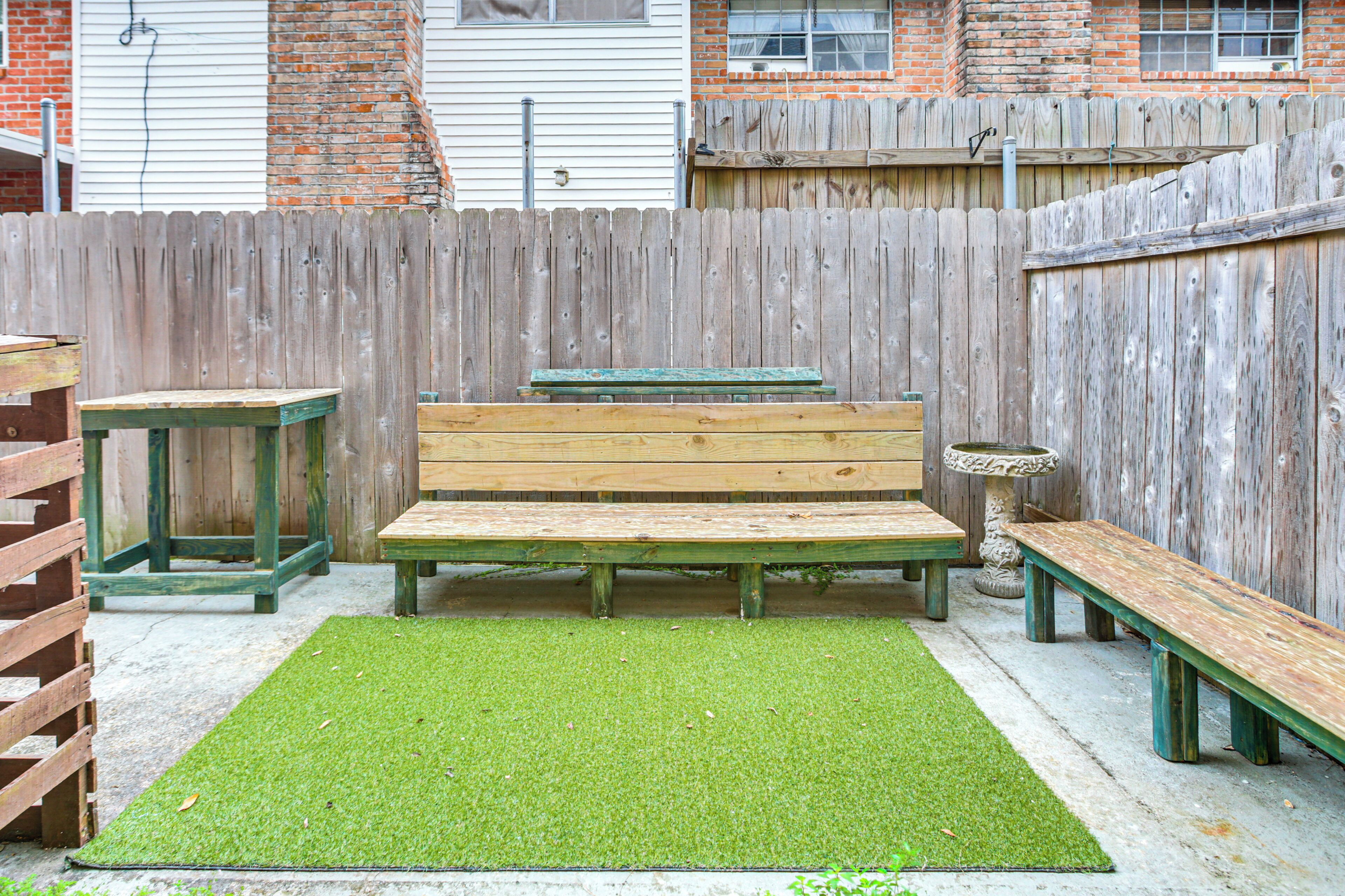 Un set tavolo e panche in legno su un prato sintetico verde in un giardino recintato da una staccionata.
