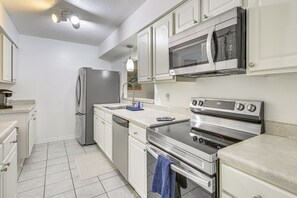 Una cucina moderna con mobili bianchi, elettrodomestici in acciaio inossidabile e pavimento piastrellato.