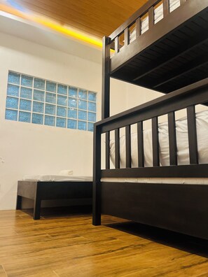 A bunk bed with a wooden frame and white bedding, a window with blue-tinted glass, and a wooden floor. - Jezette's Inn (Sipalay)