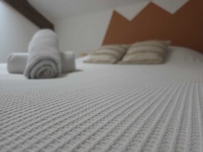 A bed with a textured white cover and neatly rolled white towels.