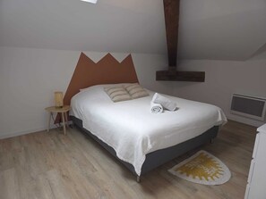 Een slaapkamer met een bed, nachtkastje, lamp, verwarming en een houten vloer.