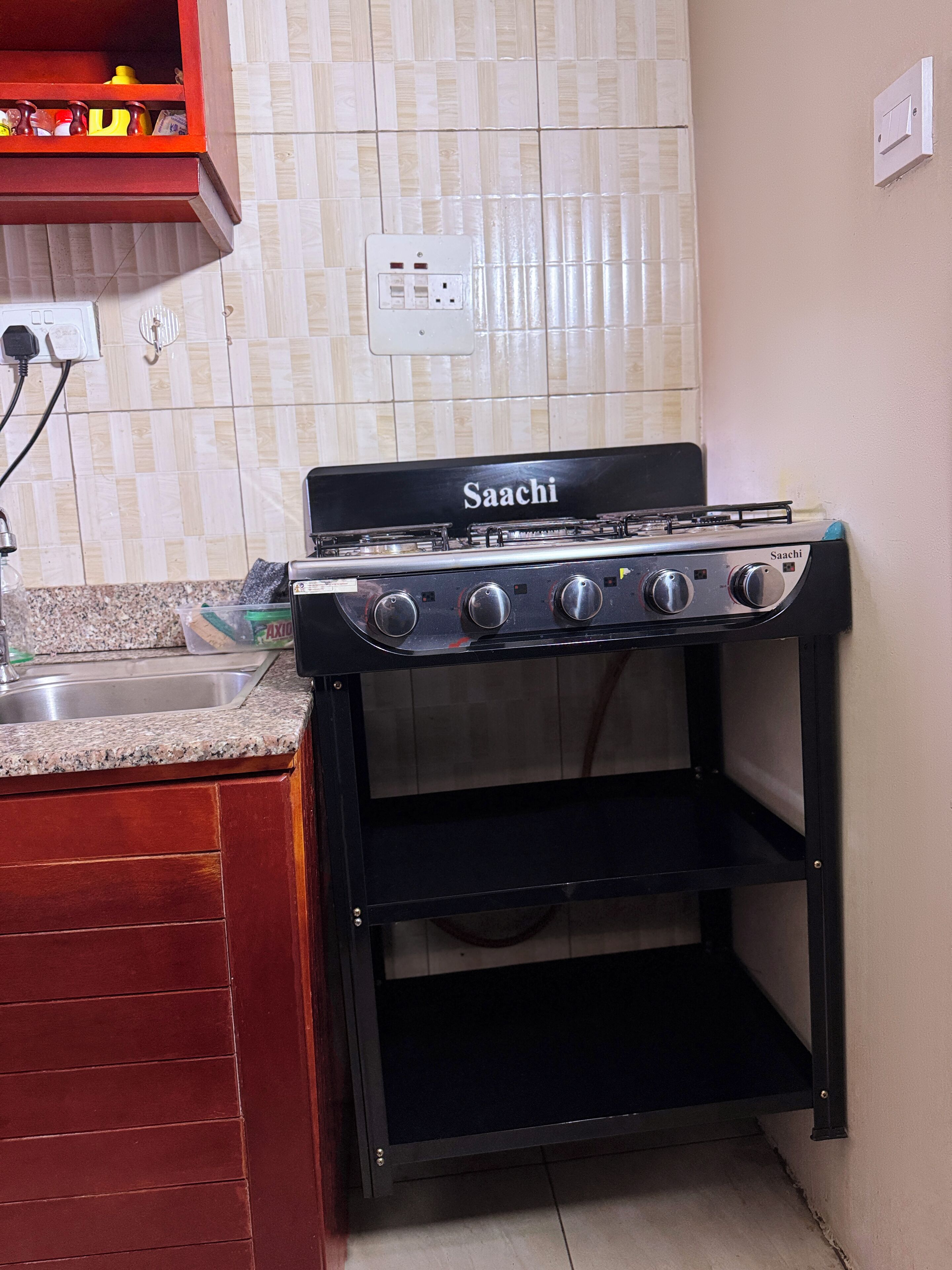 Uma cozinha compacta com um fogão a gás Saachi preto, um armário de madeira e painel de azulejos.