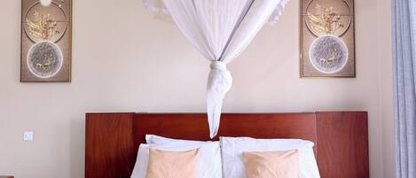 Una cama bien tendida con dosel, dos obras de arte en la pared y un cabecero de madera.