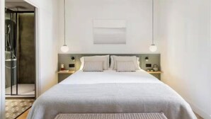 Una habitación de hotel moderna con una cama grande, dos mesitas de noche y un área de ducha.